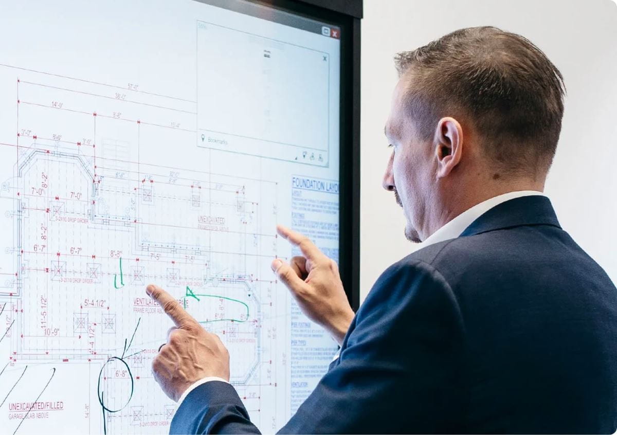 Professional working with architecture blueprints on a SMART Board using SMART Meeting Pro for seamless system integration.