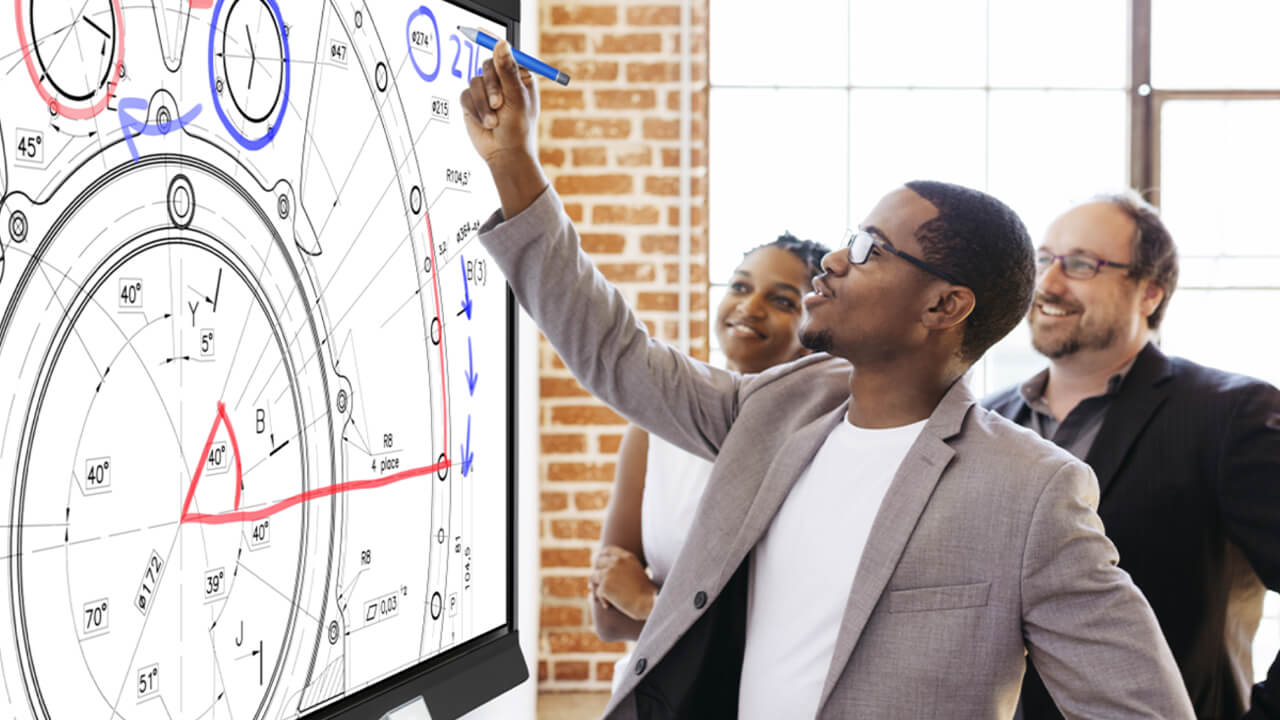 Business professional using SMART Ink to annotate a blueprint on a SMART board, with colleagues watching and smiling.